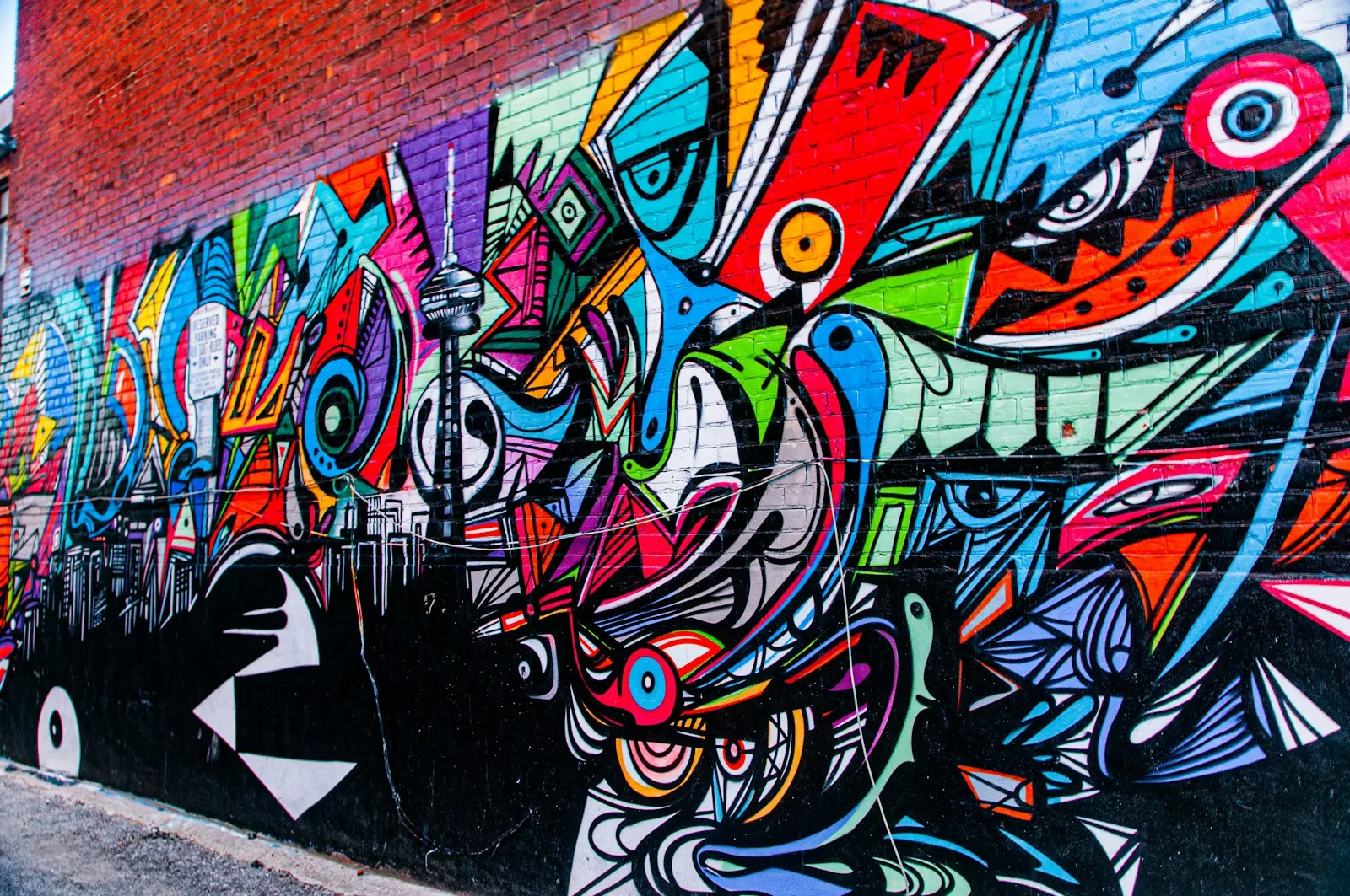 A vivid mural of abstract characters fills a brick wall with blue, pink, red, and green.